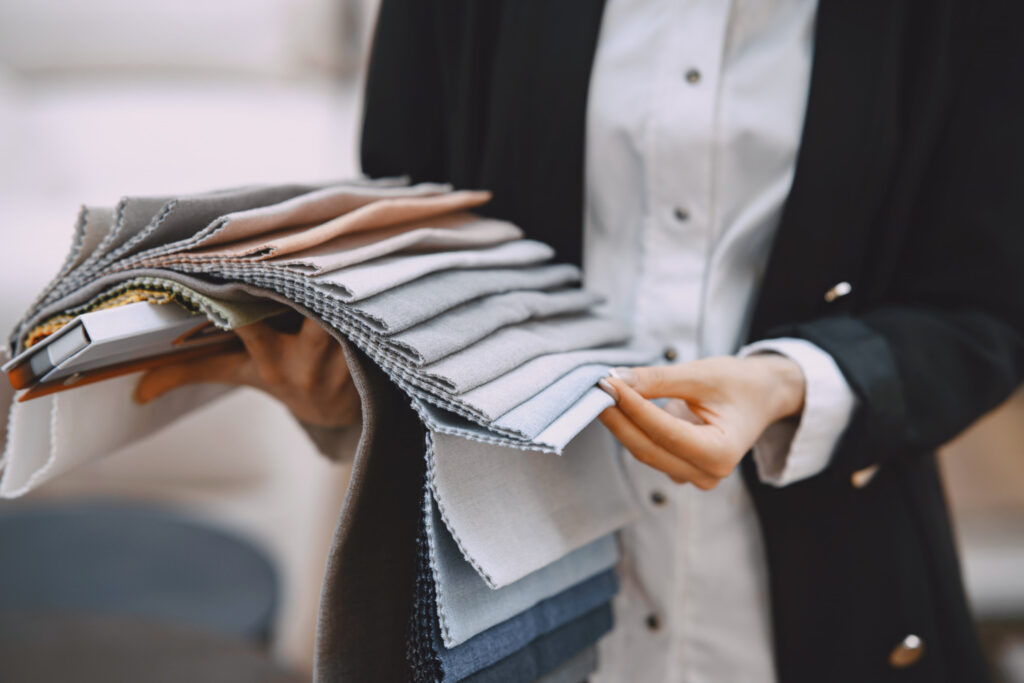 A person holding a stack of diverse fabric swatches in various colors and textures, showcasing options for design selection.